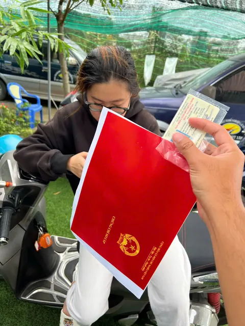 Học viên nữ cầm bìa hồ sơ đỏ, vui mừng sau khi thi